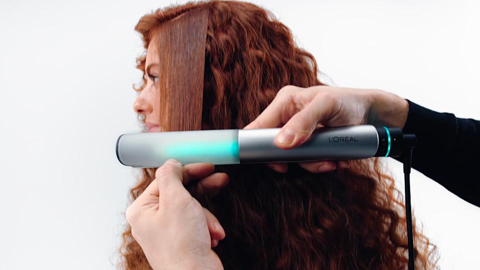 A pair of hands using the L'Oréal Light Straight and multi-styler on a person's hair. 